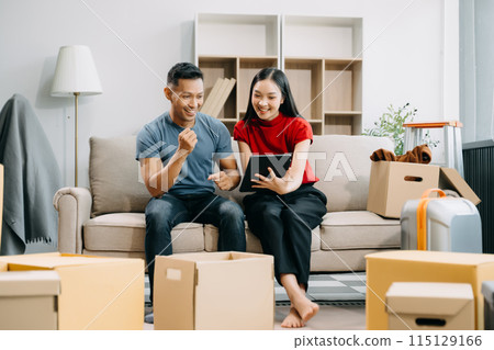 Asian young attractive couple man and woman use tablet and smartphone online shopping furniture decorate house with carton package move in new house. married asian moving home. . 115129166