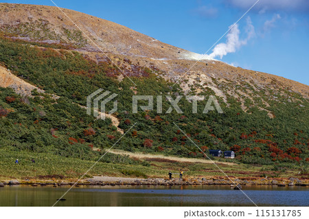 Climbers walking along Lake Kamanuma in the Azuma Mountain Range with autumn foliage and smoke rising from Mt. Issaikyo Climbers walking along Lake Kamanuma in the Azuma Mountain Range with autumn foliage and smoke rising from Mt. Issaikyo 115131785