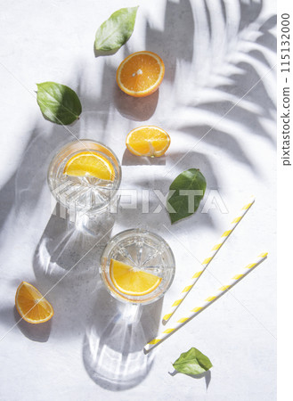 A glass of mineral water and a slice of orange on a gray table with fresh juicy fruit oranges A glass of mineral water and a slice of orange on a gray table with fresh juicy fruit oranges 115132000
