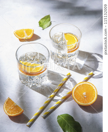 A glass of mineral water and a slice of orange on a gray table with fresh juicy fruit oranges A glass of mineral water and a slice of orange on a gray table with fresh juicy fruit oranges 115132009