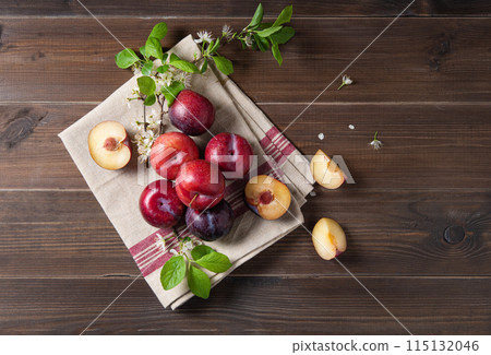 a few juicy red plums with branch blossom flowers on a napkin on a brown wood background.  115132046