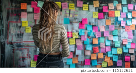 Woman Observing Colorful Paper Stickers and Sticky Notes on Wall, Back View 115132631