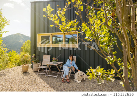 Young woman sitting relaxed near a modern house in mountains Young woman sitting relaxed near a modern house in mountains 115132636