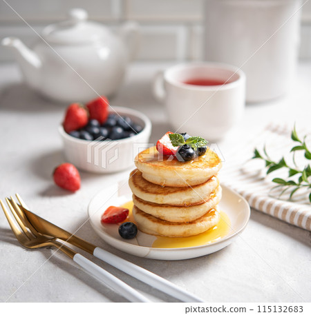 Homemade classic American pancakes in a stack with fresh berries, honey, cup of tea and pot  115132683