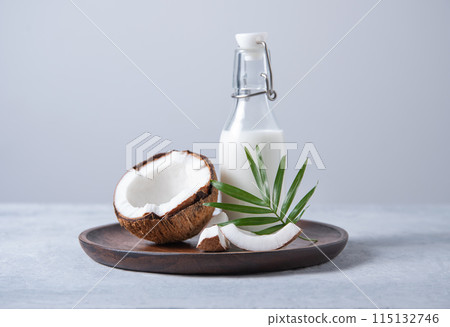 Healthy milk bottle with half coconuts and palm branch in wooden plate on blue background 115132746