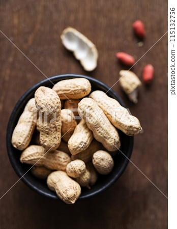 unpeeled peanuts in a black bowl on a dark wooden  background. Macro and close up image. Top view 115132756