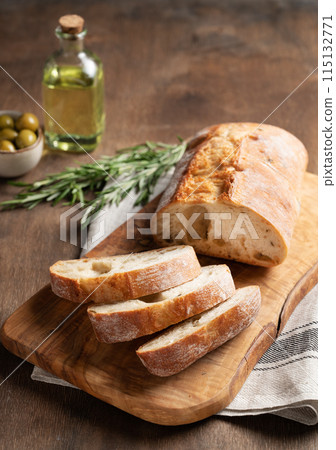 Italian fresh ciabatta bread cut slices with rosemary and olive oil on wooden background. Italian fresh ciabatta bread cut slices with rosemary and olive oil on wooden background. 115132771