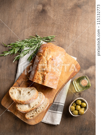 Fresh italian ciabatta bread cut  slices with rosemary and olive oil on wooden background.  115132773