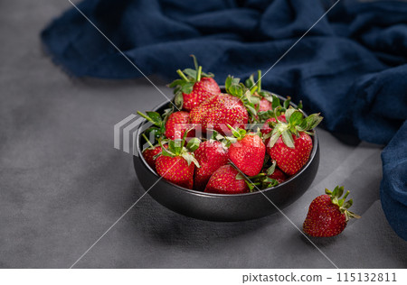 Ripe strawberries in a black bowl on a dark background with a napkin and shadows. 115132811