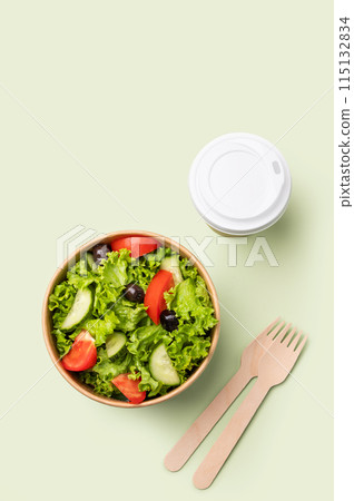 Fresh salad in eco-friendly container with wooden fork and cup on a green background. 115132834