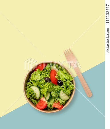 Fresh salad in eco-friendly container with wooden fork on yellow and blue background.. 115132837