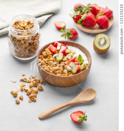 Natural yogurt with granola, kiwi and strawberries in a wooden bowl on a light background 115133210