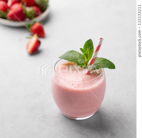 A glass of fresh strawberry smoothie on a light background with fresh berries. A glass of fresh strawberry smoothie on a light background with fresh berries. 115133211