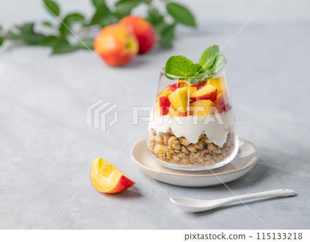 Yogurt parfait with peach and granola in a glass on a light background with fresh fruits. Yogurt parfait with peach and granola in a glass on a light background with fresh fruits. 115133218