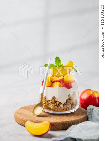 Greek yogurt parfait with peach and muesli in a glass on a wooden board on a light background 115133223