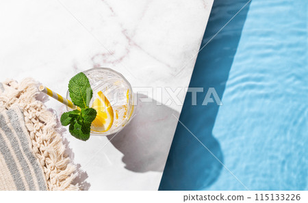 Cold lemonade in a glass with lemon, mint and ice on a marble background with the edge of a pool. Cold lemonade in a glass with lemon, mint and ice on a marble background with the edge of a pool. 115133226