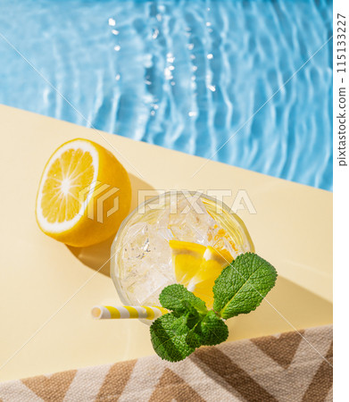 Cold lemonade in a glass with lemon, mint and ice on a yellow background with the edge of a pool Cold lemonade in a glass with lemon, mint and ice on a yellow background with the edge of a pool 115133227