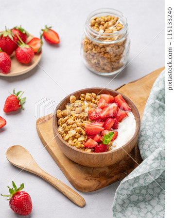 Natural yogurt with granola and strawberries in a wooden bowl on a wooden board  115133240