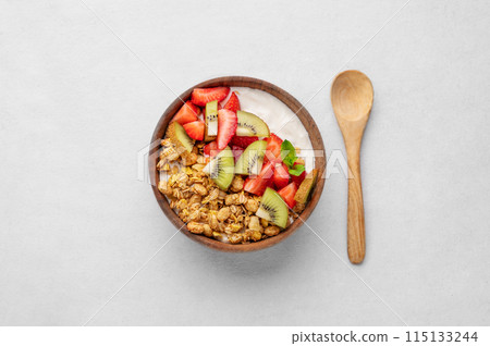 Natural yogurt with granola, kiwi and strawberries in a wooden bowl on a light background with spoon 115133244