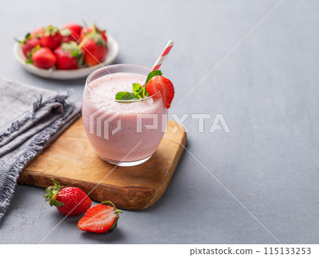 A glass of fresh strawberry smoothie with mint on a wooden board on a blue background  115133253