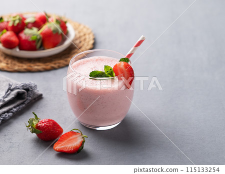 A glass of fresh strawberry smoothie with mint on a blue background with fresh berries and napkin. 115133254