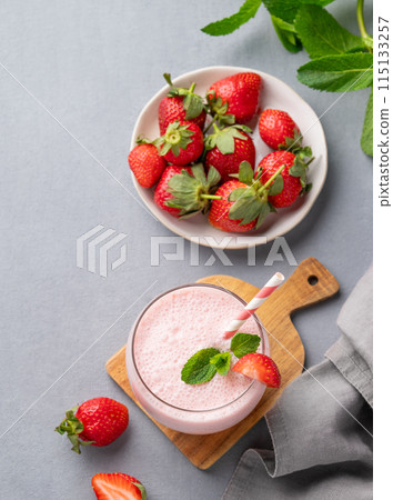 A glass of fresh strawberry smoothie with mint on a wooden board on a blue background A glass of fresh strawberry smoothie with mint on a wooden board on a blue background 115133257
