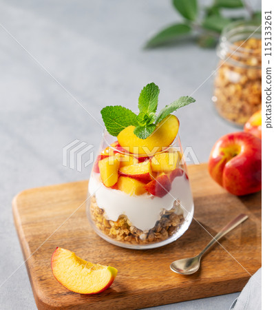 Greek yogurt parfait with peach and granola in a glass on a wooden board on a light background Greek yogurt parfait with peach and granola in a glass on a wooden board on a light background 115133261