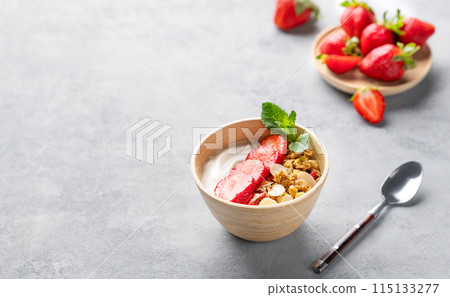 Natural greek yogurt with granola and strawberries in a bowl on a blue background with fresh berries 115133277
