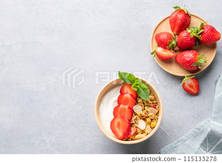 Natural yogurt with granola and strawberries in a bowl on a blue background with fresh berries  115133278