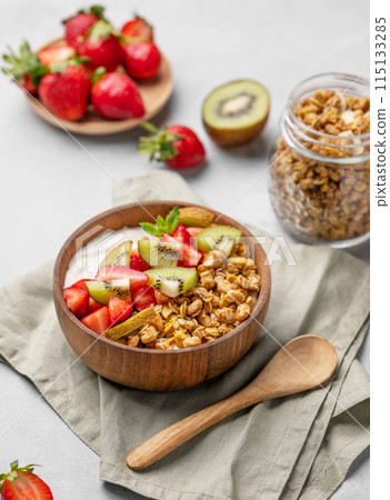 Natural yogurt with granola, kiwi and strawberries in a wooden bowl on a light background  115133285