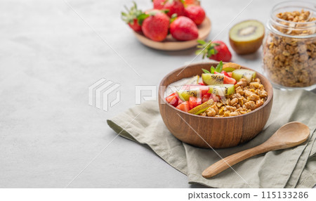 Natural yogurt with granola, kiwi and strawberries in a wooden bowl on a light background  115133286