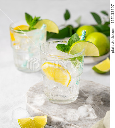 Two glasses of mojito cocktail or tonic with lemon, lime, mint and ice on a marble board. 115133307