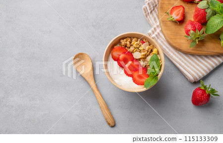 Natural yogurt with muesli and strawberries in a bowl on a blue background with berries and mint. Natural yogurt with muesli and strawberries in a bowl on a blue background with berries and mint. 115133309