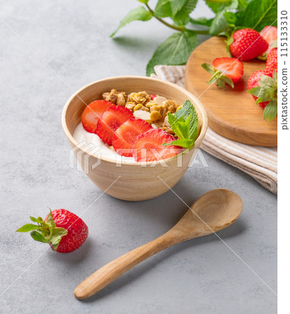 Natural yogurt with muesli and strawberries in a bowl on a blue background with berries and mint. Natural yogurt with muesli and strawberries in a bowl on a blue background with berries and mint. 115133310