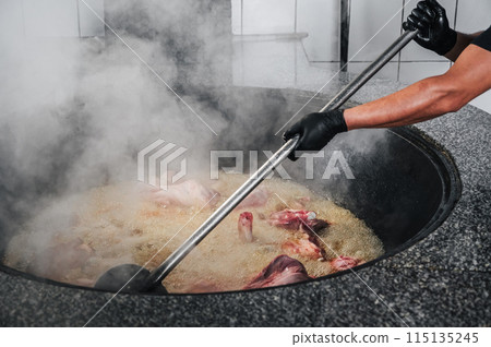 male chef cooks meat in boiling cauldron for traditional oriental Uzbek pilaf in kitchen of restaurant in Uzbekistan 115135245
