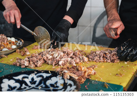 male chefs cut boiled beef meat with knives on a cutting board for cooking oriental Uzbek pilaf in kitchen at a Restaurant in Tashkent in Uzbekistan 115135303