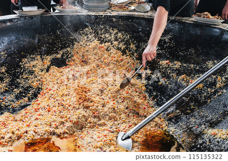 hands of a male cooking traditional oriental Arabic Uzbek pilaf in cauldron. Central Asian Pilaf Center in Uzbekistan in Tashkent hands of a male cooking traditional oriental Arabic Uzbek pilaf in cauldron. Central Asian Pilaf Center in Uzbekistan in Tashkent 115135322