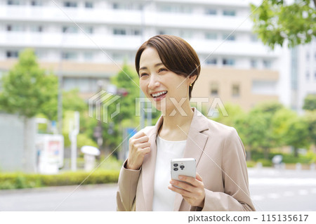 Businesswoman using a smartphone outside 115135617