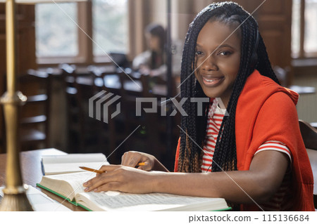 Cute african american young woman sitting at the table in the library Cute african american young woman sitting at the table in the library 115136684
