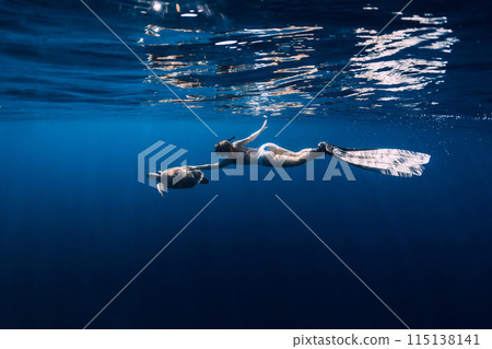 Woman snorkeling underwater and touching turtle in blue sea. Woman snorkeling underwater and touching turtle in blue sea. 115138141
