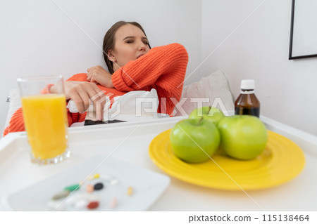 A sick teenager lying on her bed coughing, covering her mouth with an elbow. 115138464