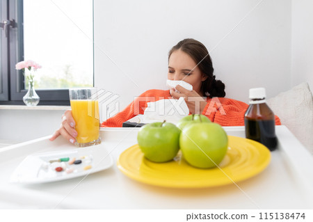 A teenager sitting on the bed snot his nose before taking the next dose of tablet medicine. 115138474