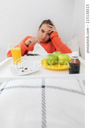 A young teenager lies on a bed and takes out handkerchiefs to blow her nose. 115138515