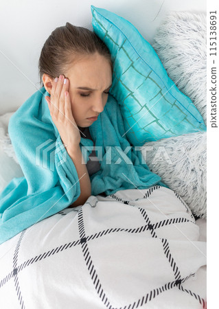 A young teenager lies in her bed because she is sick and has a chronic headache. 115138691