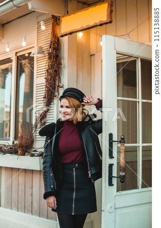 Brunette woman in black leather jacket and black hat standing outside 115138885