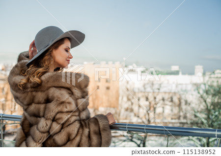 Glamorous brunette woman wearing hat and fur coat on the background of city landscape 115138952