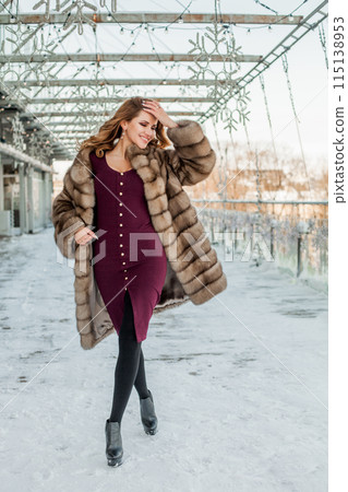 Happy brunette woman wearing fur coat standing on the street 115138953