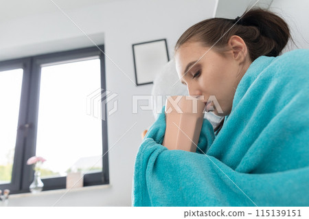 A young teenager drinks hot tea with herbs while lying on her bed under the covers. A young teenager drinks hot tea with herbs while lying on her bed under the covers. 115139151