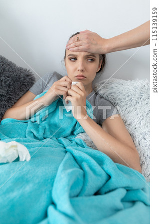 Mom touches her daughter's forehead with her hand, checking if the high temperature still persists. 115139159