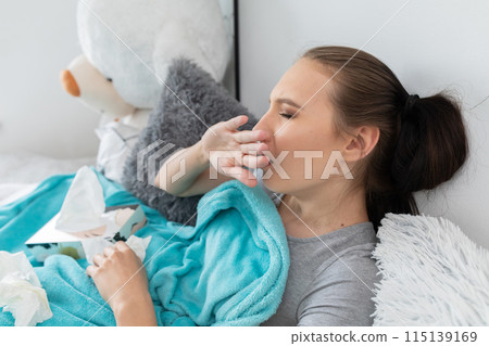 A teenager coughing strongly, cutting her mouth with her hand, lying in her bed under a warm blanket. 115139169